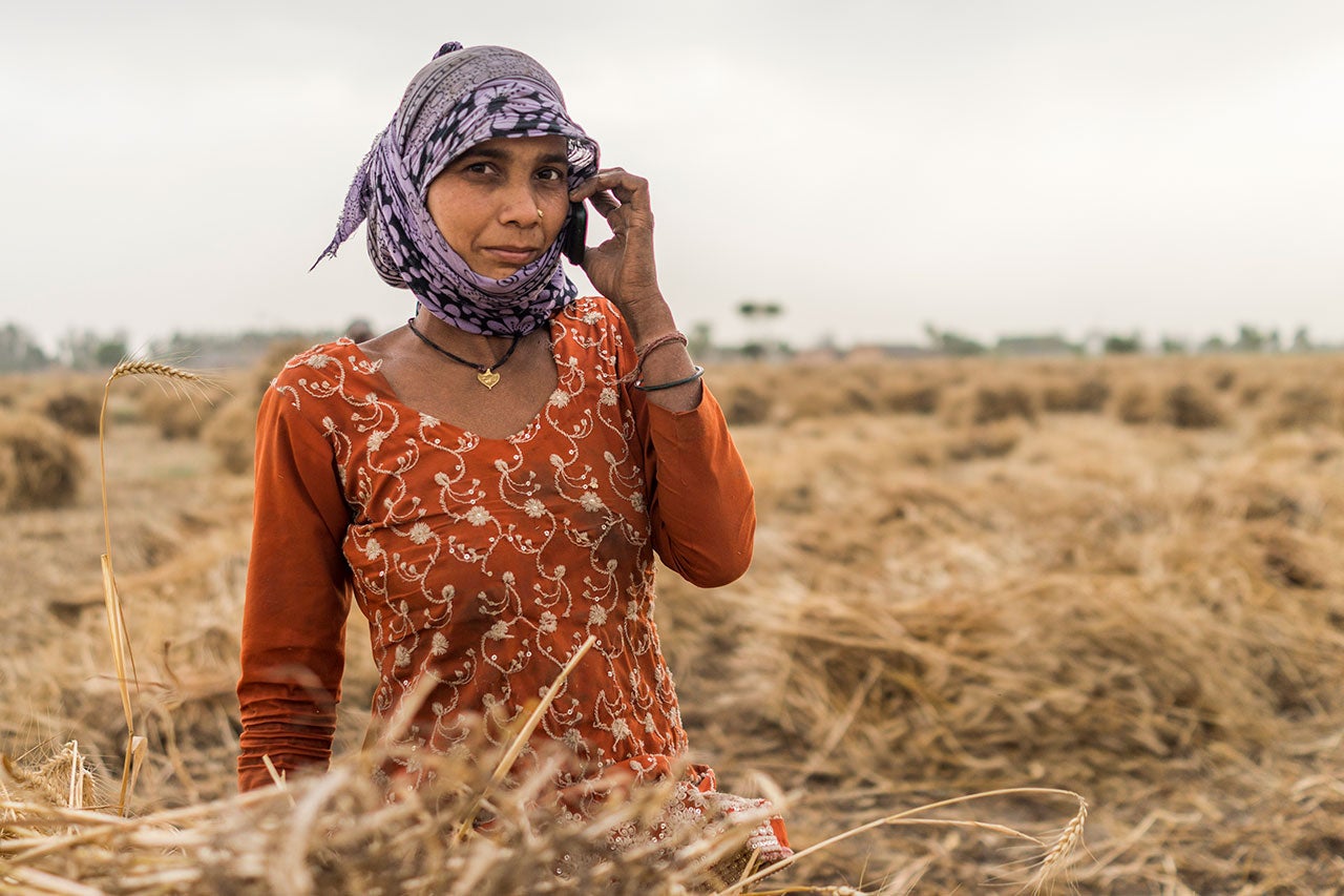 A woman stands in a field and raises a cell phone to her ear.